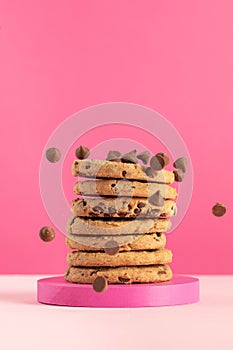 Chocolate chip cookies stacked on pink with falling chips. Bakery.