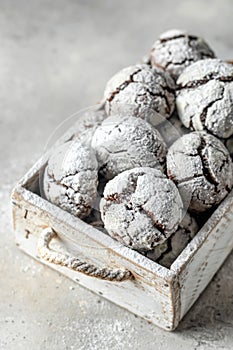 Chocolate chip cracked cookies close up. Wooden rustic box with fresh baked chocolate crinkle cookies in icing sugar on