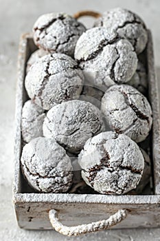 Chocolate chip cracked cookies close up. Wooden rustic box with fresh baked chocolate crinkle cookies in icing sugar on