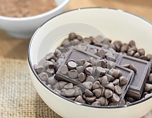 Chocolate chips and Dark chocolate bar in white bowl.