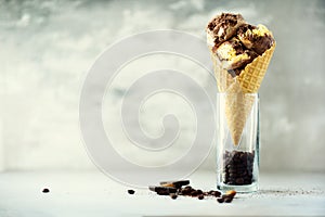 Chocolate and coffee ice cream in waffle cone with coffee beans on grey stone background. Summer food concept, copy