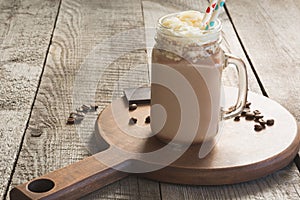 Chocolate coffee milkshake with whipped cream served in glass mason jar on vintage wooden background. Sweet drink.