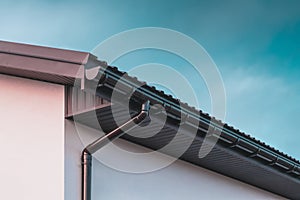 Chocolate-colored plastic gutter on the roof of the building and downpipe on the wall