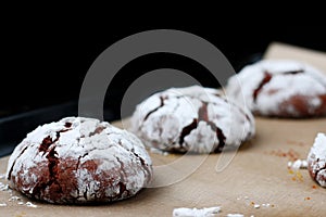 Chocolate cookies with cracks on baking paper and iolated on black. Cracked chocolate biscuits