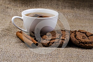 Chocolate cookies with a cup of tea and cinnamon on a burlap