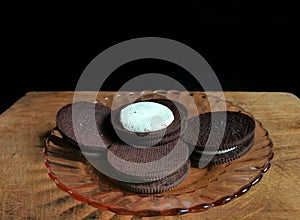 Chocolate cookies filled with cream on a glass plate on wooden table with black background. food concept