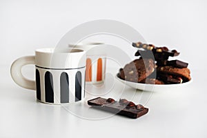 Chocolate cookies with chocolate slices and nuts on a plate next to two cups of tea