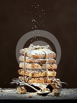 Chocolate cookies in a stack tied with a rope are sprinkled with powdered sugar on a brown background.