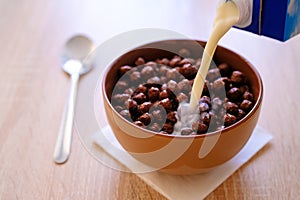 Chocolate corn balls in milk for Breakfast. Pouring milk with splashes of drops into a bowl of crispy Breakfast cereals rich in