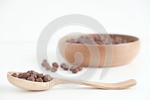 Chocolate corn balls in a wooden bowl and spoon on a white background. Copy, empty space for text