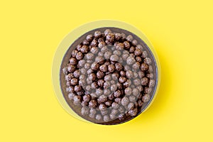 Chocolate corn flakes in a bowl on a yellow isolated background in the center of the image