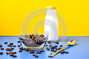 Chocolate cornflakes in the shape of letters of the English alphabet for a quick breakfast with milk in bottle on color background