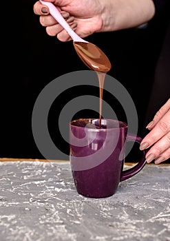 Chocolate cream in a cup with silino lacatka in the hands of a pastry chef. Melted milk chocolate on a dark background