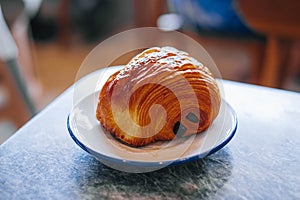 Chocolate croissant or pain au chocolat in a white small plate in a marble table