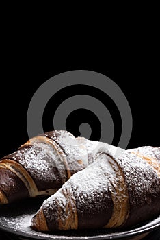 Chocolate croissants with powdered sugar on a black background.