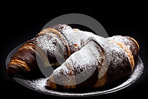 Chocolate croissants with sugar powder on a black background, close-up. French cuisine concept
