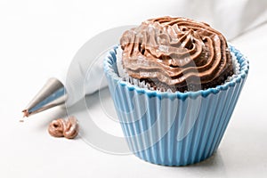 Chocolate cup cake with ganache chocolate cream and piping bag in the background on the white marble background