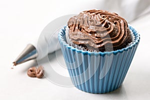 Chocolate cup cake with ganache chocolate cream and piping bag in the background on the white marble background