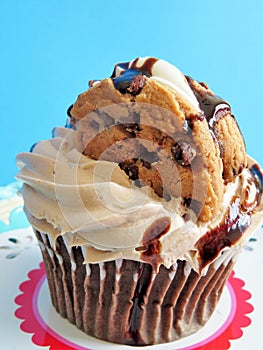 Chocolate cupcake with chocolate frosting and chocolate syrup and topped with a chocolate chip cookie