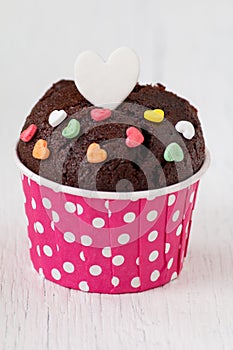 Chocolate cupcake with heart candy on white wooden table