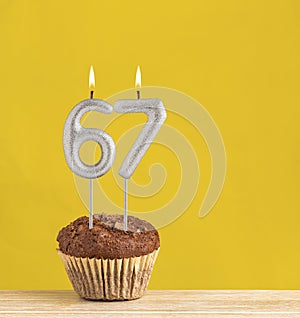 Chocolate cupcake with number 67 candle - Birthday on a yellow background