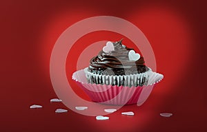 Chocolate cupcake with pink eatable hearts on red background