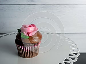 Chocolate cupcake with a pink rose bloom on top of chocolate frosting
