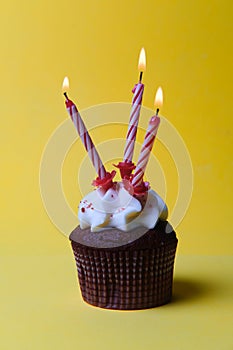Chocolate cupcake with white cream and three candles on a yellow background