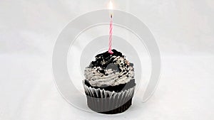 Chocolate cupcake with white frosting and a pink candle being lit and then blown out