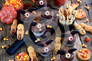 Chocolate cupcakes `bats` and shortbread cookies `witch`s fingers` - delicious bakery sweets for the celebration of Halloween.