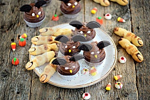 Chocolate cupcakes `bats` and shortbread cookies `witch`s fingers` - delicious bakery sweets for the celebration of Halloween.