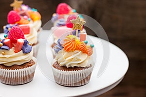 Chocolate cupcakes with cream cheese frosting, chewing marmalade, sweets and golden topper on dark background