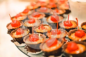 CHOCOLATE DESSERT WITH A CHERRY ON TOP IN A STRAIGHT ARRANGEMENT FOR A WEDDING DESSERT TABLE FULL OF CANDY AND PASTRY