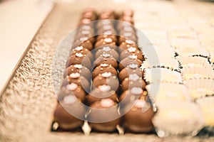 CHOCOLATE DESSERT WITH PINK FLOWERS ON TOP AND A PEARL IN THE MIDDLE IN A STRAIGHT ARRANGEMENT FOR A WEDDING DESSERT TABLE FULL OF