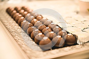 CHOCOLATE DESSERT WITH PINK FLOWERS ON TOP AND A PEARL IN THE MIDDLE IN A STRAIGHT ARRANGEMENT FOR A WEDDING DESSERT TABLE FULL OF