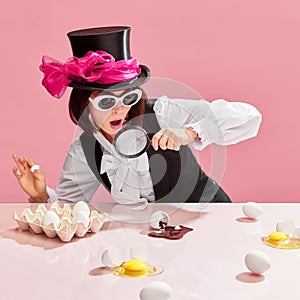 Chocolate detective. Emotional woman in cylinder and sunglasses looking in magnifying glass on egg with chocolate