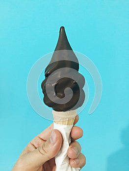 Chocolate-dipped soft-serve ice cream cone in hand against teal wall