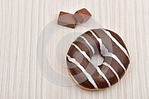 Chocolate donut with stripes and piece of chocolate on white woo