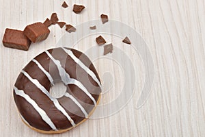 Chocolate donut with stripes and pieces of chocolate on white wooden table. Sweets. Selective focus