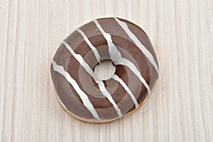 Chocolate donut with stripes on white wooden table. Sweets. Selective focus