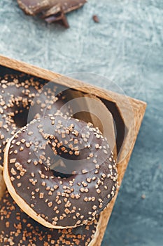 Chocolate donuts in a wooden box on a grey textured background