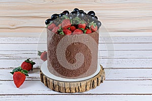 Chocolate dressed cake, decorated with grapes and strawberries, on a white wooden table