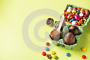 Chocolate Easter eggs with cream filling and colorful candies on a green background. Top view