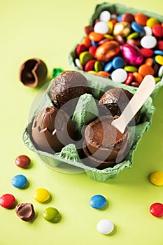 Chocolate Easter eggs with cream filling and colorful candies on a green background. Top view
