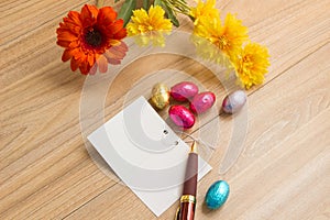 Chocolate Easter Eggs Over Wooden background with blessing card with pen and flowers on wood table