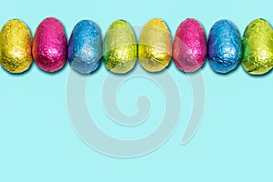 Chocolate Easter eggs wrapped in foil. Colorful Easter egg border.