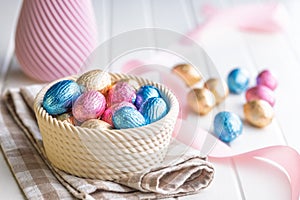 Chocolate easter eggs wrapped in multi colored foil in bowl on white table