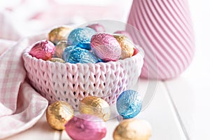 Chocolate easter eggs wrapped in multi colored foil in bowl on white table