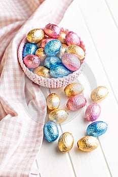 Chocolate easter eggs wrapped in multi colored foil in bowl on white table