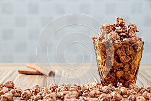 Chocolate flavored popcorn in the yellow glass and on the brown wood table with cinnamon background